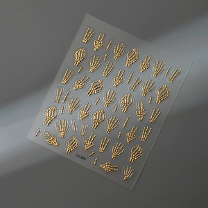 Detailed view of 3D embossed gold skeleton hand nail art stickers on a grey surface