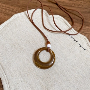 Close-up of amber resin ring pendant with wood beads on a rustic linen pouch backdrop