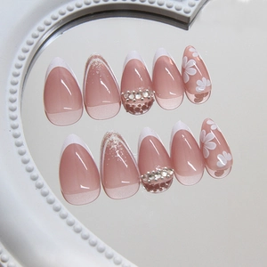 Pink French almond press-on nails with white floral patterns and sparkling rhinestones
