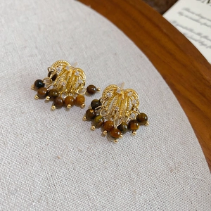 Detailed shot of golden fan-shaped tiger eye earrings with tassel beads on linen