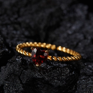 Close-up of a heart-shaped red gemstone ring with a twisted gold band on volcanic rock