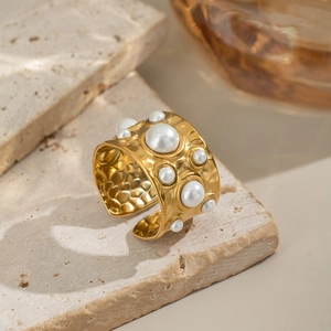 Bague large dorée texturée avec perles incrustées sur une surface en pierre