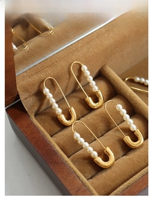Macro detail of paperclip-shaped gold earrings with white pearls in a velvet box