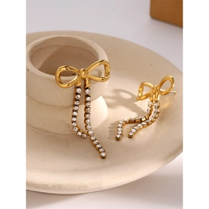 Detail of 18k gold plated bow earrings with sparkling rhinestone tassels on ceramic