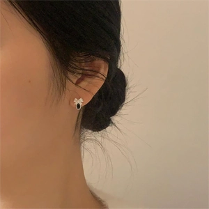 Detail view of a black oval stone earring with white flower accent on model's ear