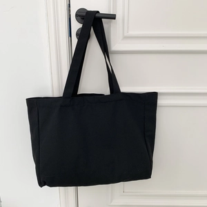 Detail of a black canvas tote bag hanging on a minimalist white door with black handle