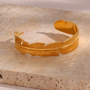 Macro detail of golden feather open bangle with clear metallic texture on stone