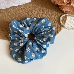 Blue knit scrunchie with white floral embroidery and elegant pleated fabric design