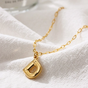 Close-up of golden letter D bubble pendant on a paperclip chain over white fabric