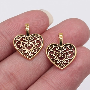Detailed view of two gold heart-shaped pendants with intricate openwork patterns on a finger