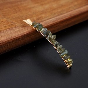 Detail of natural green crystal stone hairpin with gold metal clip on wooden tray