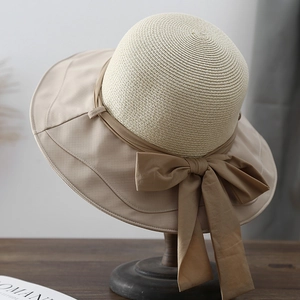 Women's wide brim straw sun hat with large bow on a vintage wooden stand