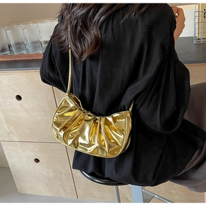 Detailed view of shiny gold pleated cloud bag worn as a shoulder bag on black silk top