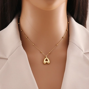 Detail of 3D bubble letter A gold pendant necklace worn on neck with bead chain