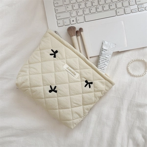 Detailed close-up of cream quilted cosmetic bag with black embroidered bows on a desk
