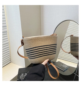 Detail view of hand-woven straw bucket bag featuring black stripes and leather strap