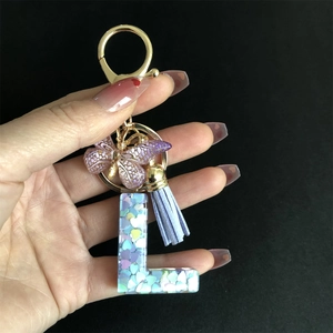 Detail of resin letter L keychain with purple butterfly, blue tassel and gold heart sequins