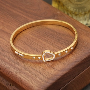 Close-up of golden bangle with hollow heart design and sparkling white zircons on wood