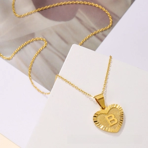 Macro shot of gold heart-shaped pendant with letter B engraving on a thin link chain