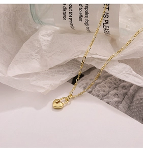 Macro detail of golden Figaro chain with a polished heart-shaped padlock pendant