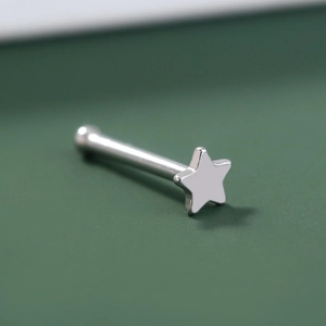 Close-up of a silver stainless steel star nose stud on a textured green background