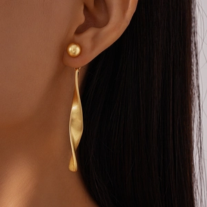 Detail of a matte gold twisted linear earring worn by a model in a close-up shot