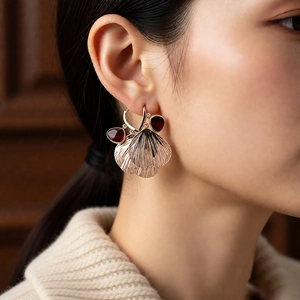 Detail of vintage gold earrings with ribbed textures and deep red teardrop glass stones