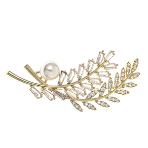 Elegant gold leaf brooch with cubic zirconia crystals and a white pearl on white background