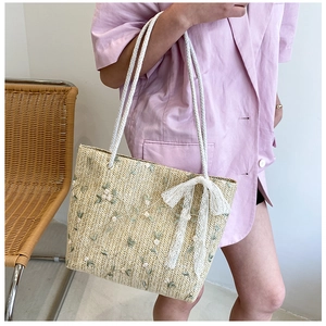 Detail of straw tote bag featuring delicate floral embroidery and white lace bow decoration
