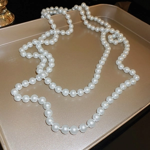 Elegant vintage long white pearl necklace displayed on a beige tray for layering