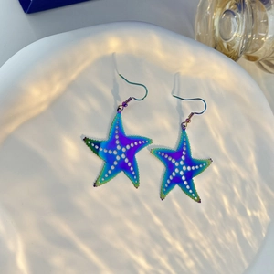 Macro shot of colorful iridescent starfish earrings on white tray with water ripples