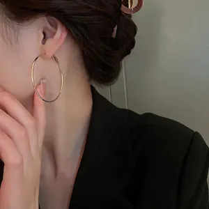 Grandes créoles dorées minimalistes pour femmes portées par un mannequin en tailleur