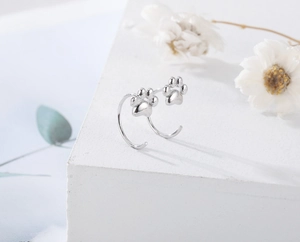 Macro shot of silver cat paw drop earrings on white geometric block with floral decor