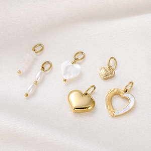 Detailed view of gold heart pendants with pearls and shells on white silk background