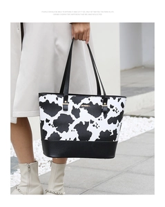 Détail du sac cabas imprimé vache avec logo doré et bordure noire porté par mannequin
