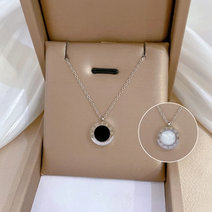 Dettaglio macro del ciondolo con numeri romani bianchi e neri su collana in acciaio