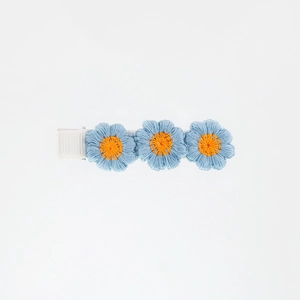Detail shot of three blue embroidered flowers with orange centers on a fabric hair clip