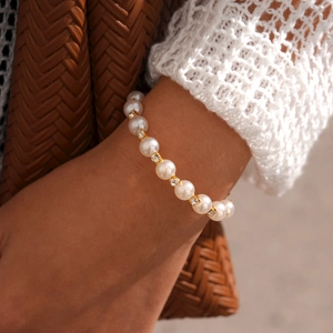 Détail d'un bracelet en perles blanches avec des entretoises dorées serties de strass