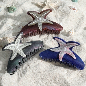Trois pinces à cheveux étoile de mer avec perles et strass sur fond de plage de sable
