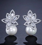 Macro detail of leaf-shaped zircon earrings with elegant white pearls on dark background