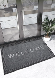 Détail du paillasson Welcome gris foncé avec texture antidérapante à l'entrée vitrée