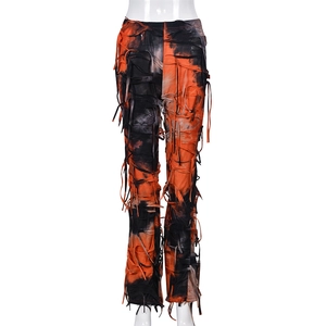 Dettaglio dei pantaloni svasati tie-dye arancioni e neri con frange effetto consumato
