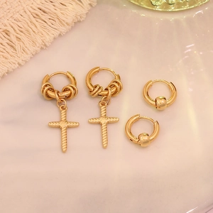 Detail of gold titanium steel cross pendant hoops and beaded earring set on white surface