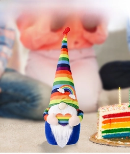 Rainbow gnome plush toy with striped hat holding a heart in a festive party setting