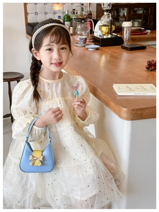 Detail of cream tulle girl's dress with gold stars and blue bow handbag in warm cafe
