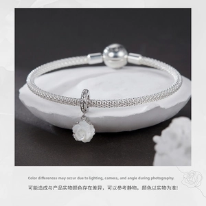 Close-up of white rose charm on silver mesh bracelet over a minimalist stone base
