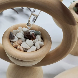 Close-up of essential oil being dropped onto colorful stones inside a wooden aroma diffuser ring