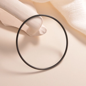 Detail view of a 2mm slim black stainless steel bangle on a minimalist beige background