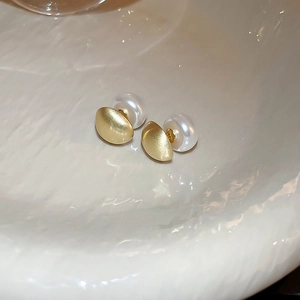 Close-up of gold matte geometric earrings with lustrous white pearls on a soft background