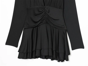 Detail of black long sleeve dress featuring waist pleats and layered ruffle hem